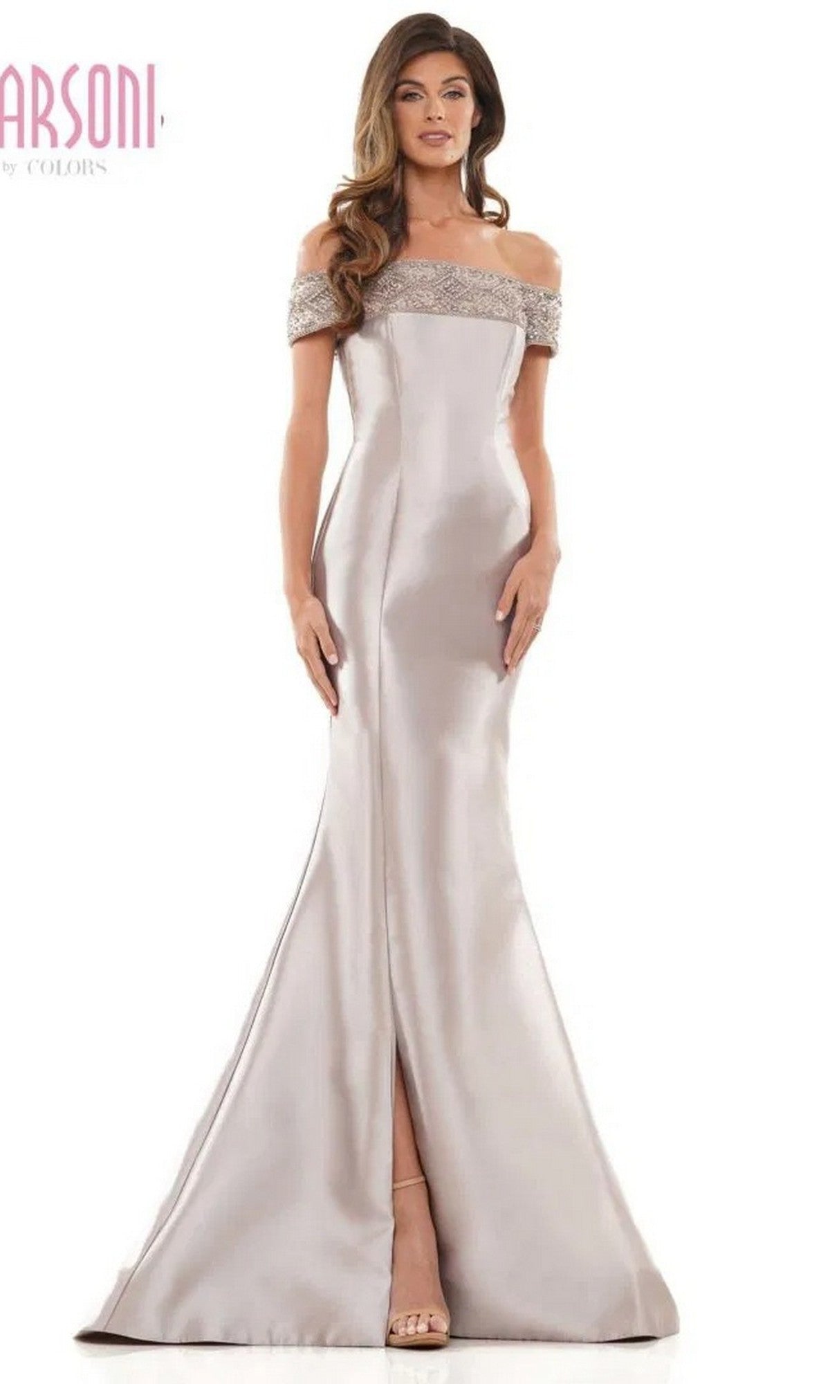 A woman stands against a plain background wearing the Long Formal Dress: Marsoni MV1184 in taupe, featuring a floor-length mermaid skirt with front slit, off-shoulder neckline, and beaded trim.